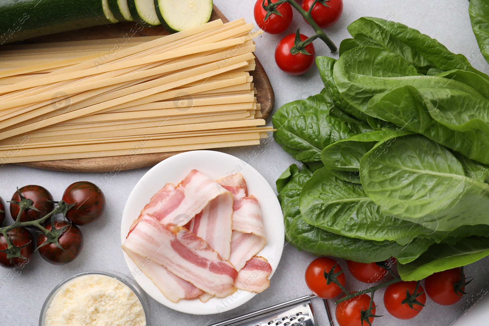 Photo of Raw pasta, bacon and fresh ingredients on light grey table, flat lay