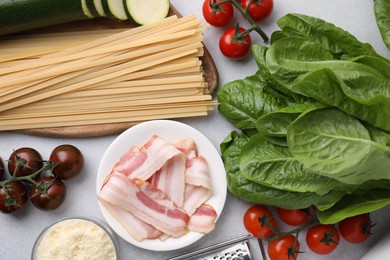 Photo of Raw pasta, bacon and fresh ingredients on light grey table, flat lay