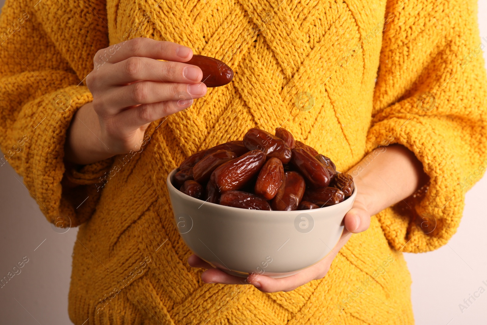 Photo of Woman with bowl of tasty sweet dried dates on light background, closeup