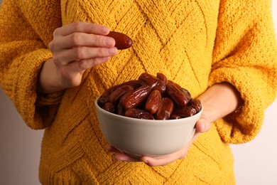 Woman with bowl of tasty sweet dried dates on light background, closeup