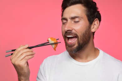 Photo of Handsome man eating tasty sushi with chopsticks on pink background