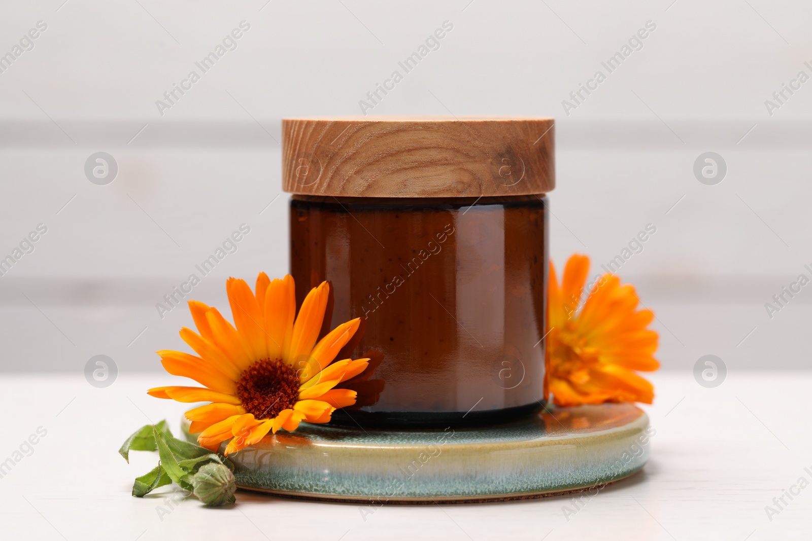 Photo of Jar of cosmetic product and beautiful calendula flowers on white table, closeup