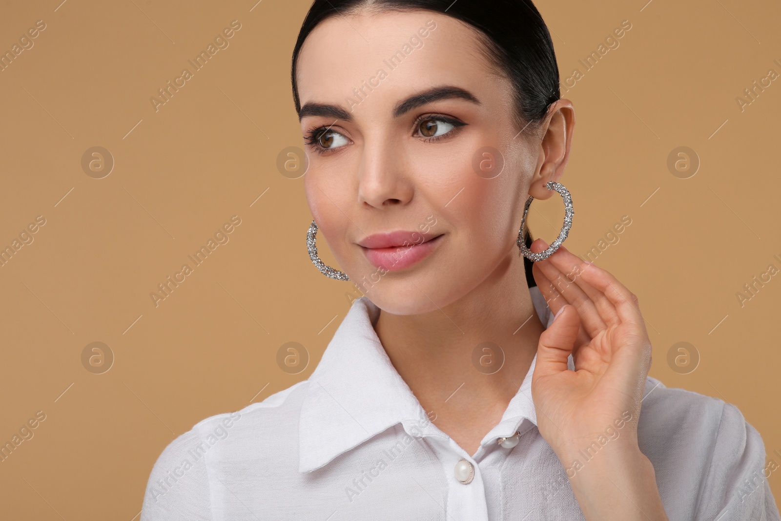 Photo of Beautiful young woman with elegant earrings on beige background