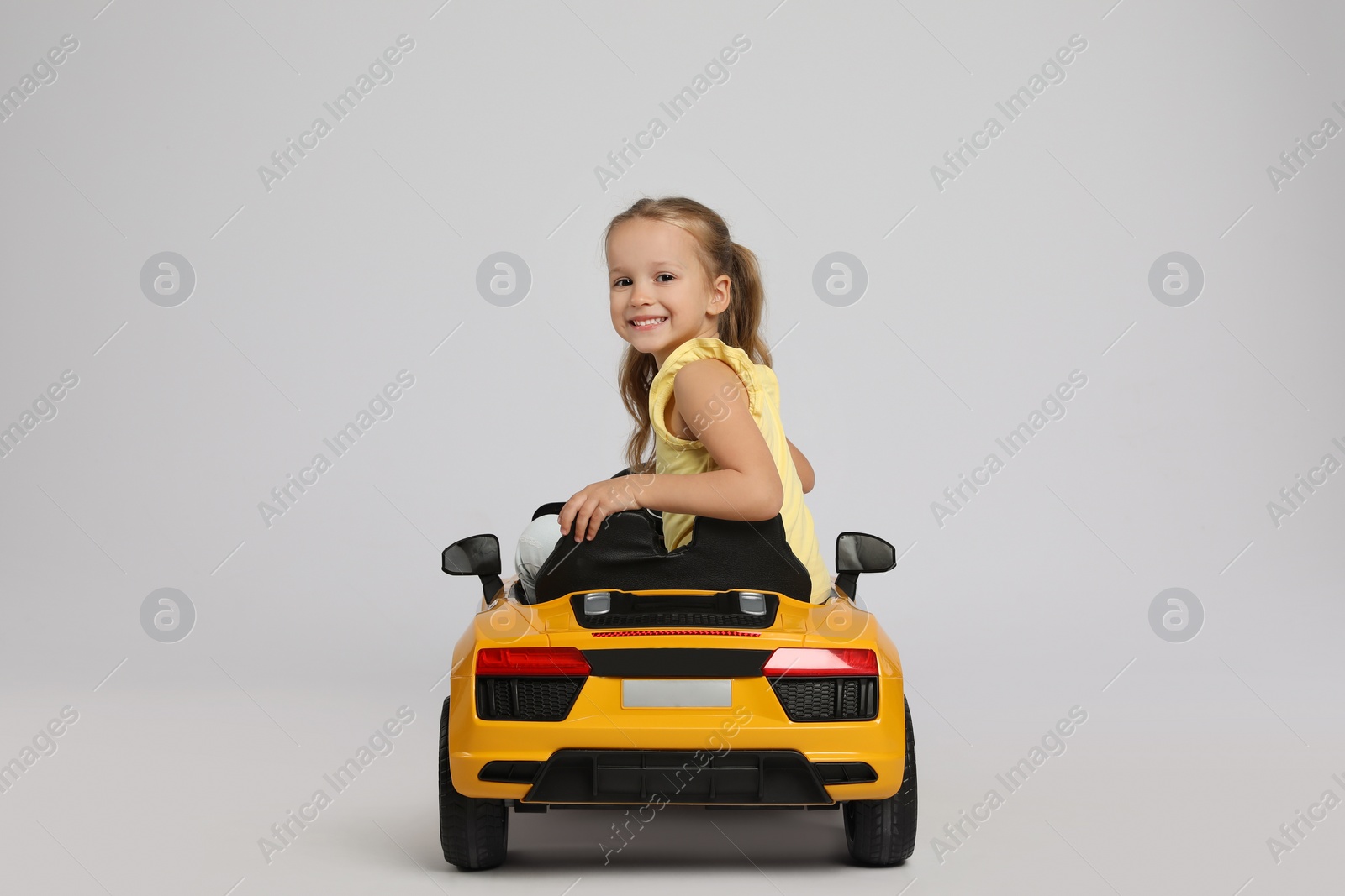Photo of Cute little girl driving children's electric toy car on grey background