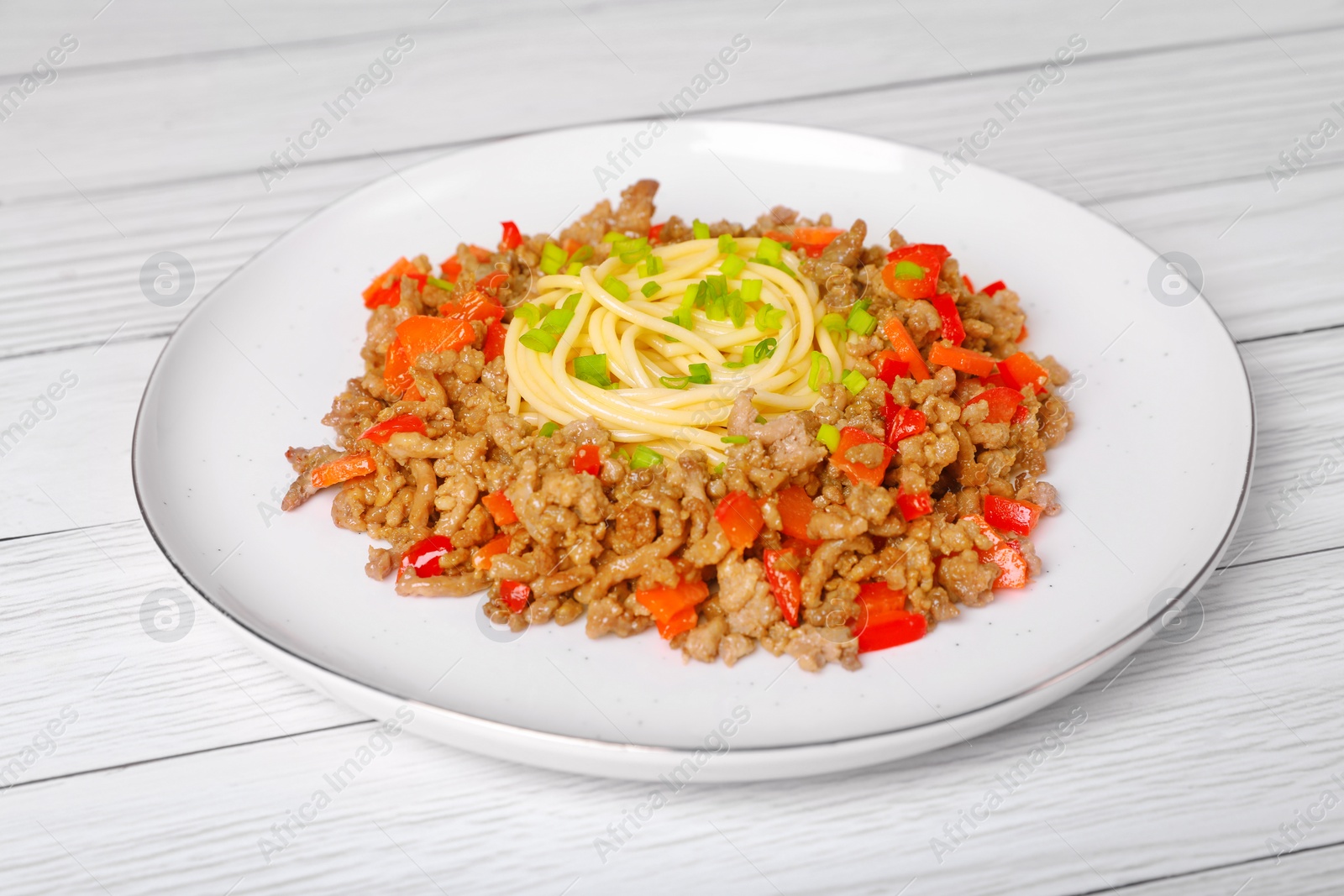Photo of Tasty minced meat with spaghetti, vegetables and green onion on white wooden table, closeup