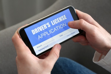 Photo of Man holding smartphone with driver's license application form at home, closeup