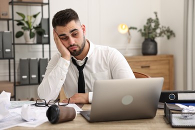 Photo of Overwhelmed man sitting at table with laptop and documents in office