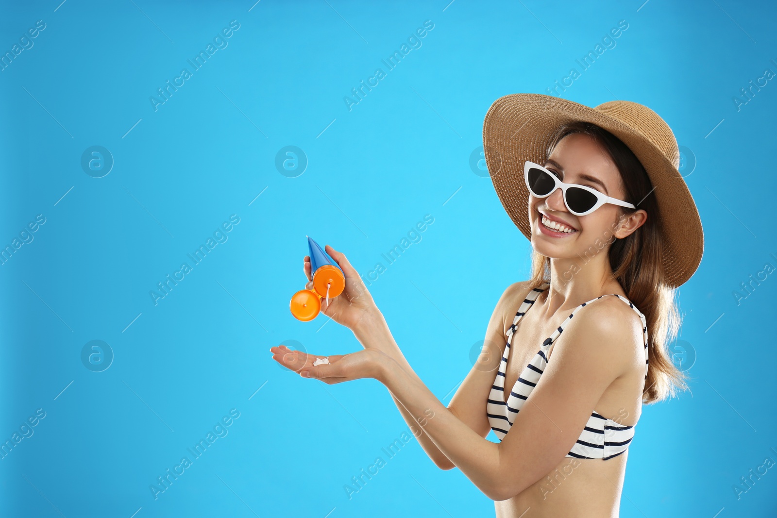 Photo of Young woman applying sun protection cream on light blue background. Space for text