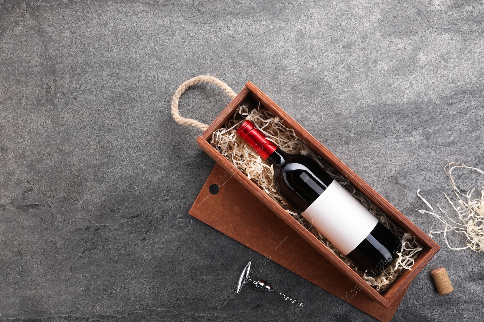 Photo of Bottle of wine in wooden box and corkscrew on dark textured table, flat lay. Space for text