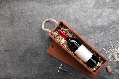 Photo of Bottle of wine in wooden box and corkscrew on dark textured table, flat lay. Space for text