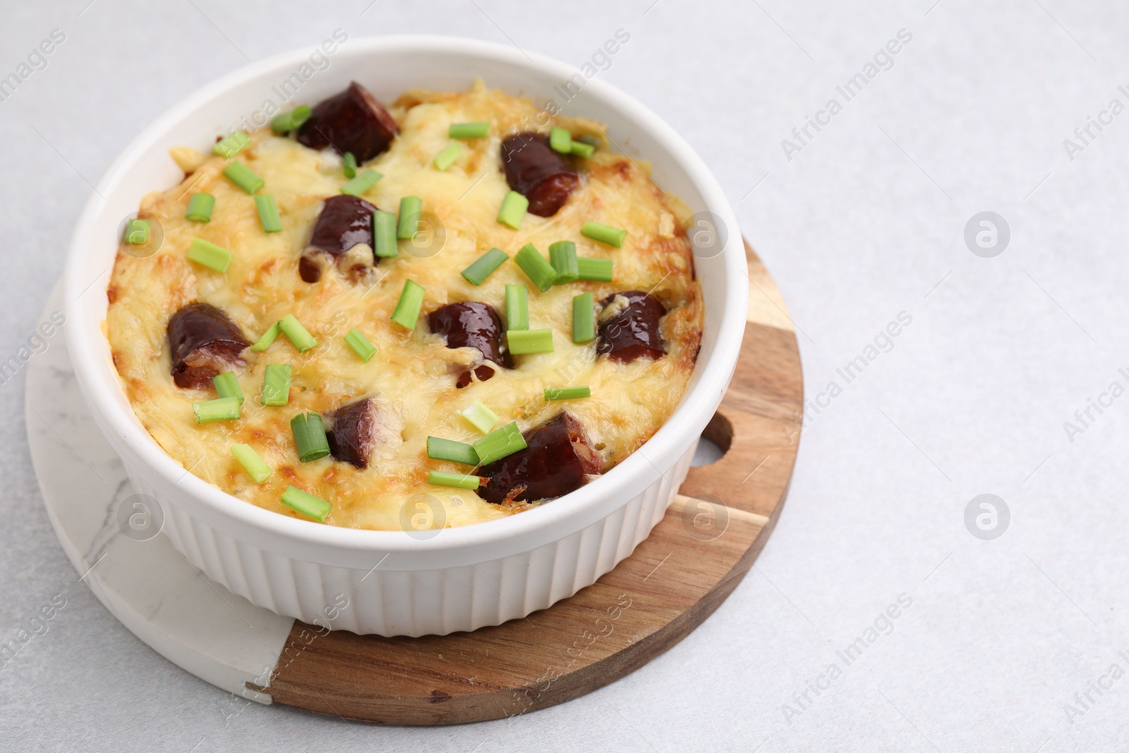 Photo of Tasty sausage casserole with green onions in baking dish on white table, closeup