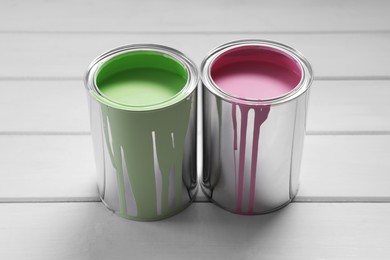 Photo of Cans of pink and green paints on white wooden table