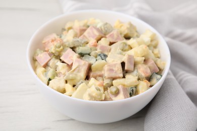 Photo of Tasty Olivier salad with boiled sausage in bowl on white table, closeup