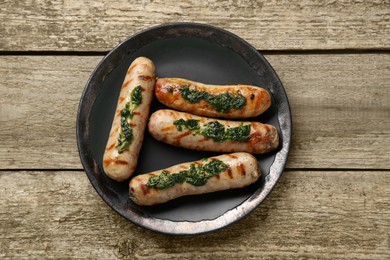 Photo of Tasty fresh grilled sausages with sauce on wooden table, top view