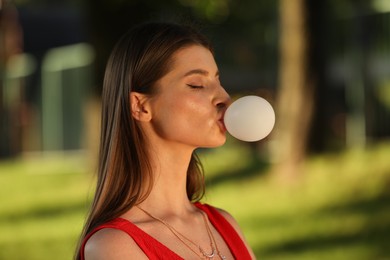 Photo of Beautiful young woman blowing bubble gum in park
