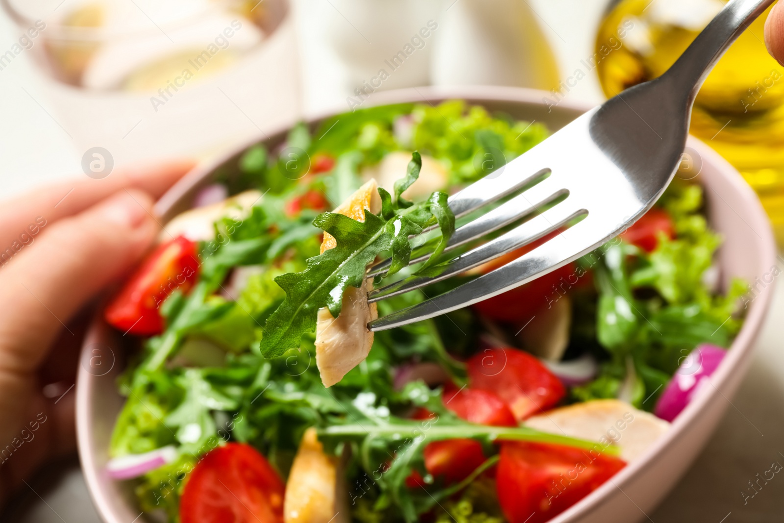 Photo of Woman eating delicious salad with chicken, arugula and tomatoes at table, closeup