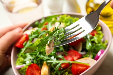 Woman eating delicious salad with chicken, arugula and tomatoes at table, closeup