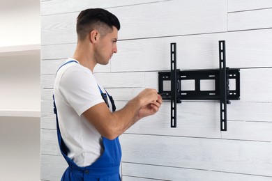 Photo of Professional technician with screwdriver installing TV bracket on wall indoors