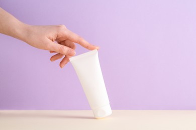 Woman with tube of cream on lilac background, closeup