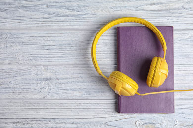 Photo of Book and modern headphones on white wooden table, top view. Space for text