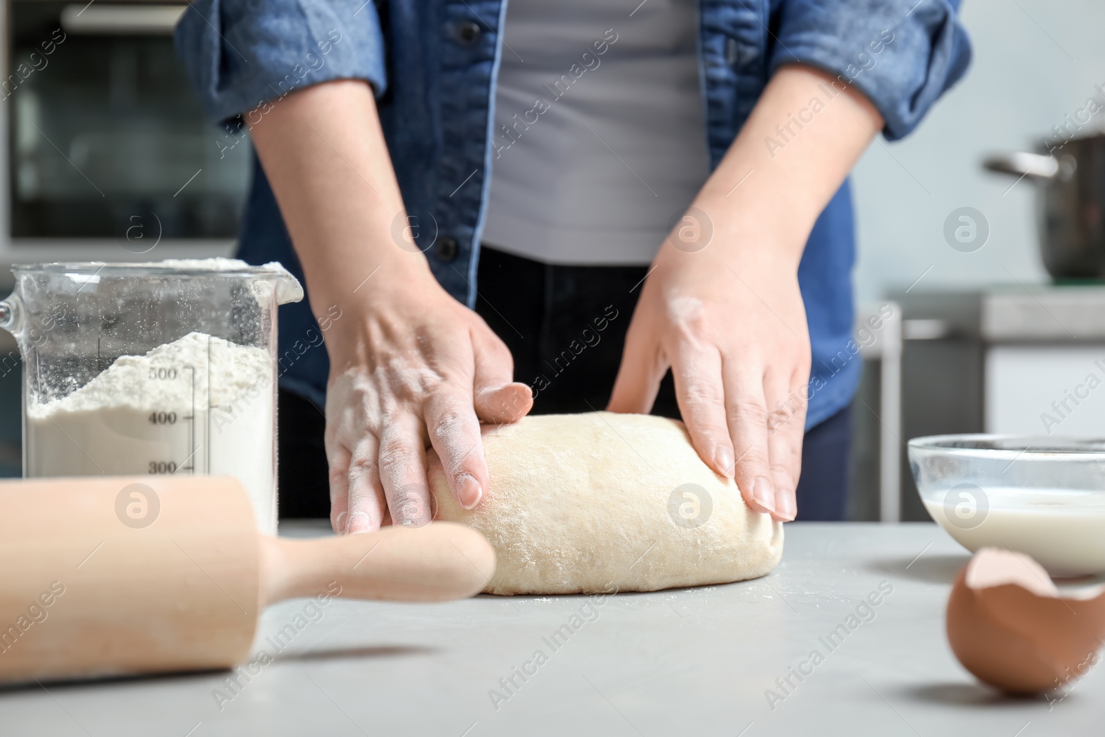 Photo of Woman kneading dough near graduated jug with flour on table in kitchen