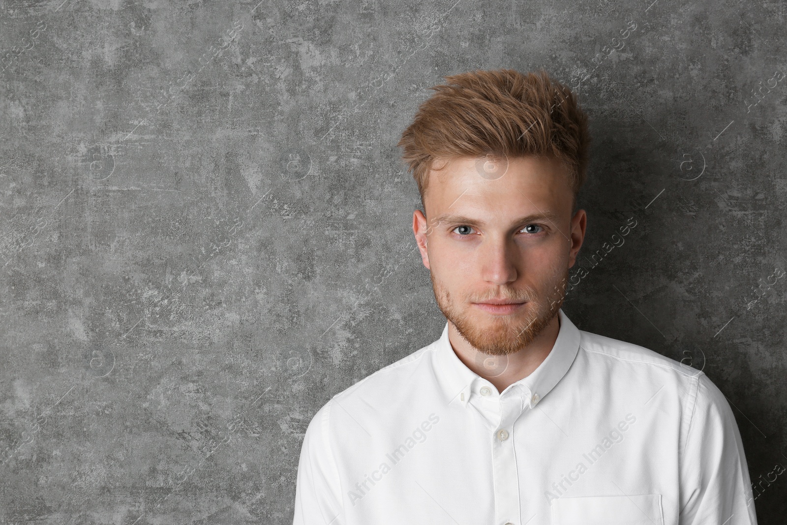 Photo of Portrait of handsome young man near grey wall. Space for text