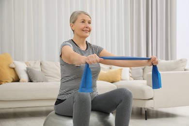 Senior woman doing exercise with elastic resistance band on fitness ball at home