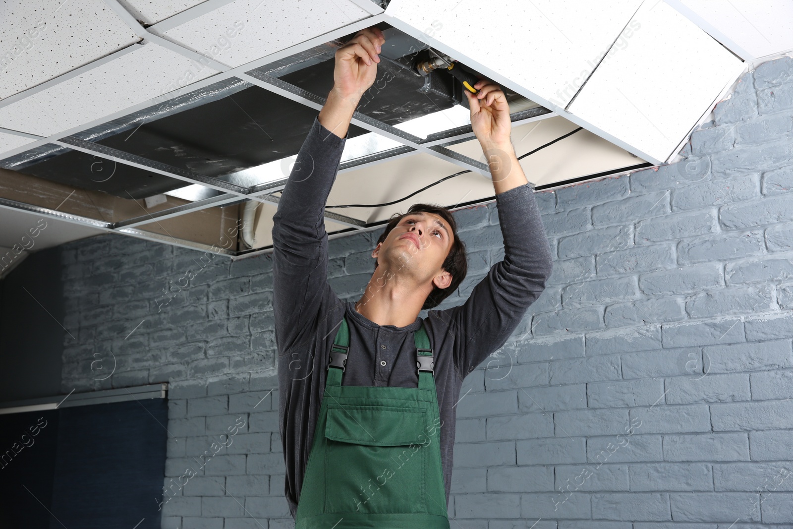 Photo of Young male technician repairing air conditioner indoors