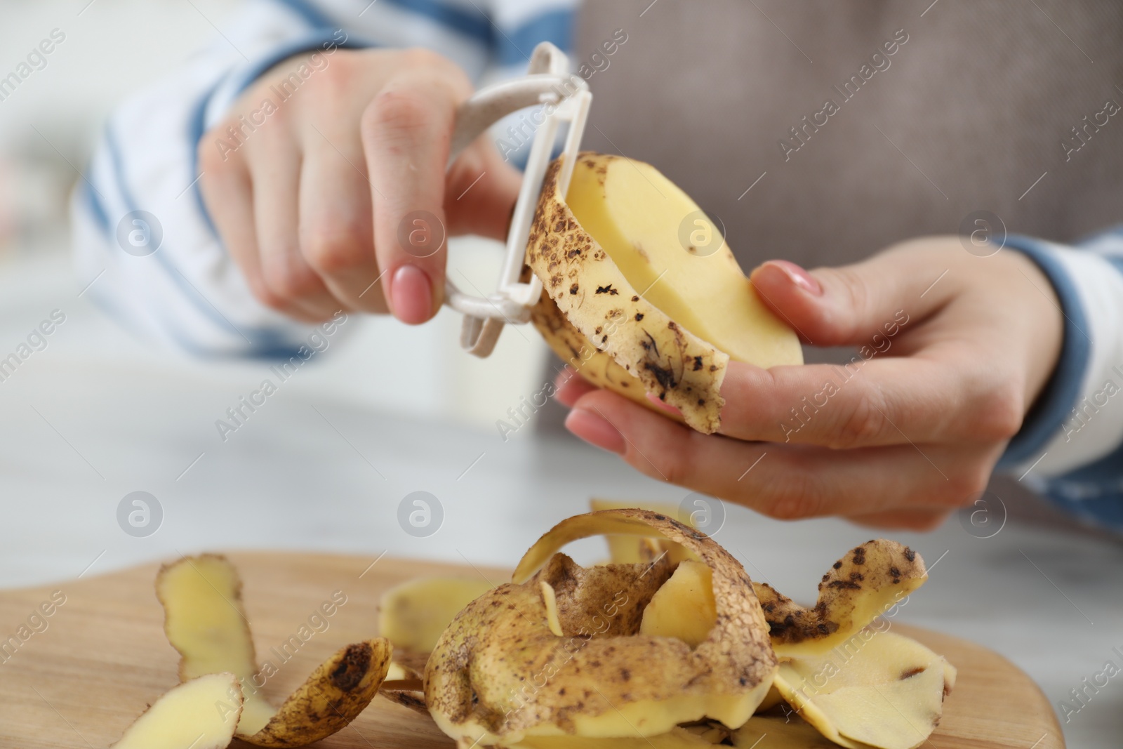 Photo of Woman peeling fresh potato at white table, closeup