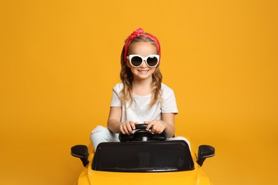 Cute little girl driving children's electric toy car on yellow background