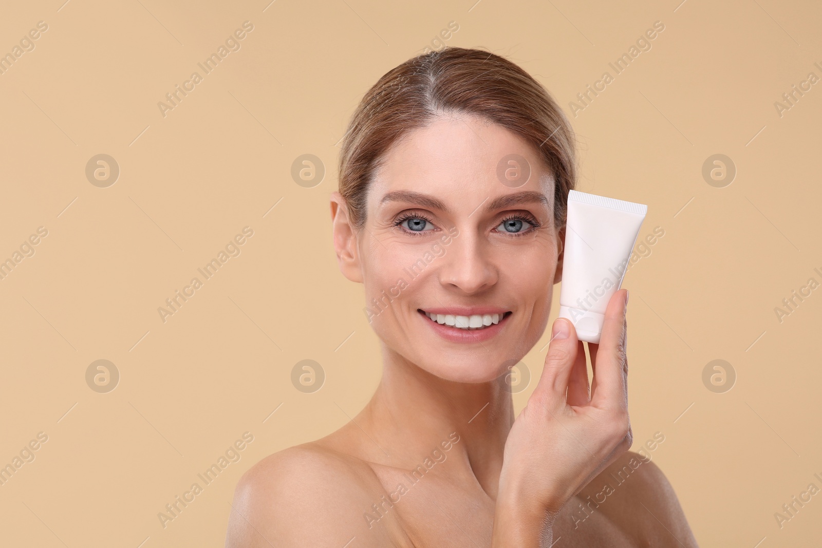 Photo of Woman holding tube of foundation on beige background