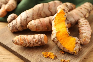 Many raw turmeric roots on wooden table, closeup