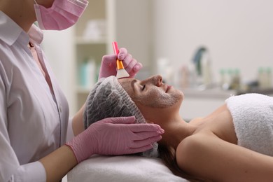 Photo of Cosmetologist applying mask on woman's face in clinic, closeup