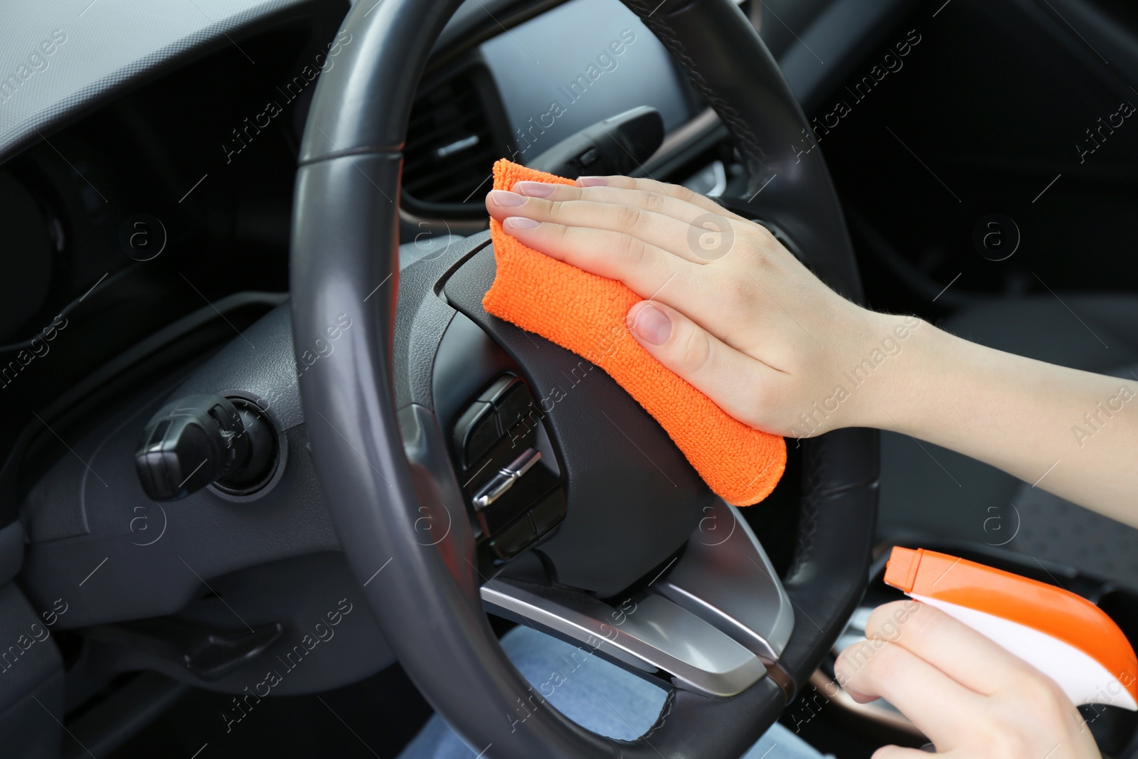 Photo of Woman cleaning steering wheel with rag in car, closeup