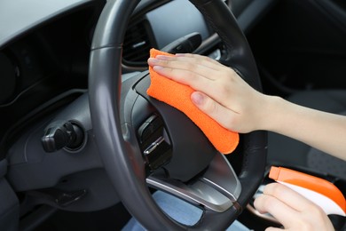 Woman cleaning steering wheel with rag in car, closeup