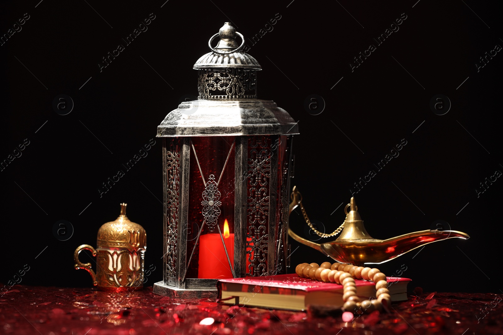 Photo of Arabic lantern, Quran, misbaha and Aladdin magic lamp on shiny red table