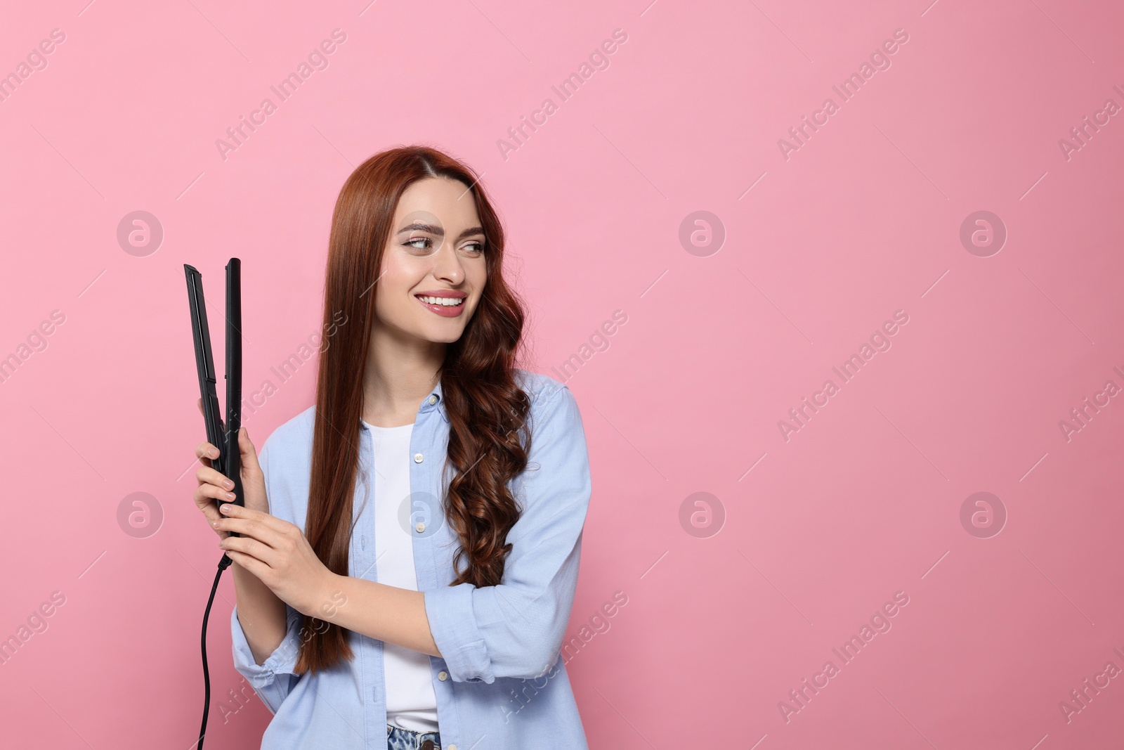 Photo of Beautiful woman with hair iron on pink background, space for text