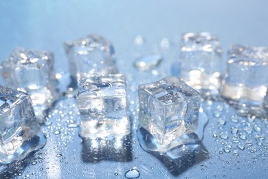 Photo of Melting ice cubes and water drops on light blue background, closeup