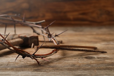 Photo of Crown of thorns and nails on wooden table, closeup with space for text. Easter attributes