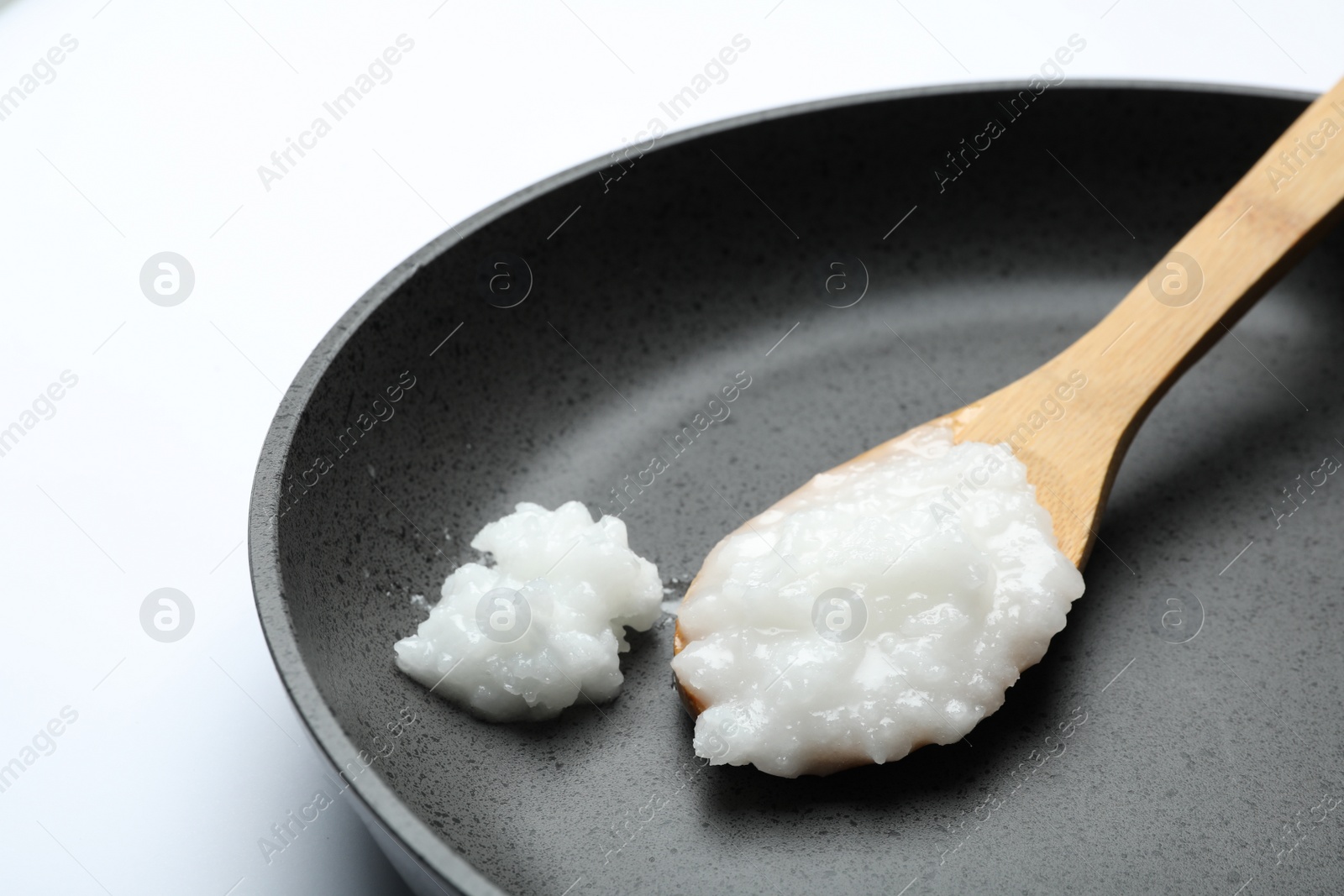 Photo of Frying pan with coconut oil and wooden spoon on white background, closeup. Healthy cooking