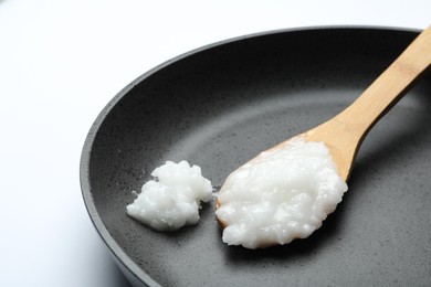 Frying pan with coconut oil and wooden spoon on white background, closeup. Healthy cooking