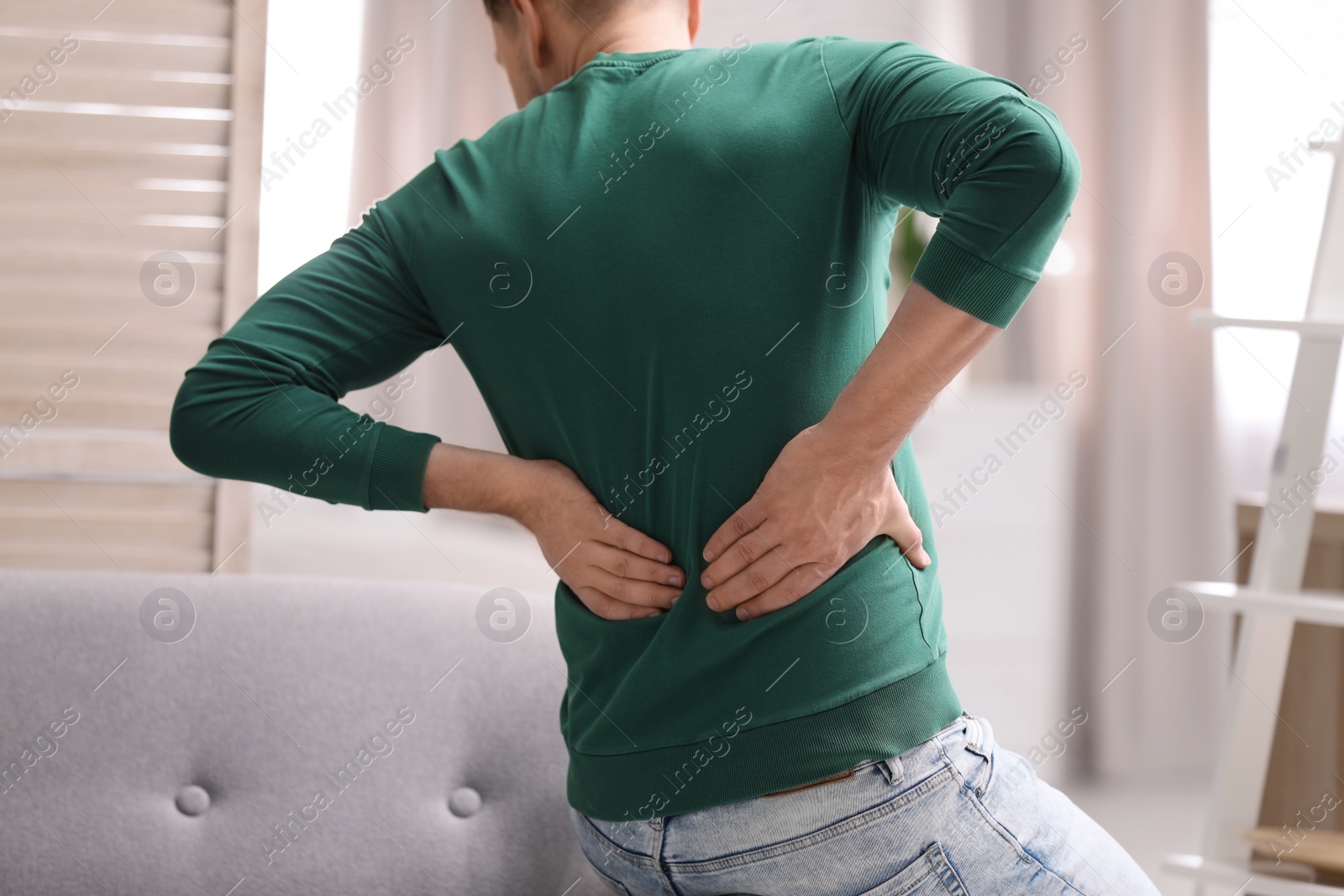 Photo of Young man suffering from back pain at home, closeup