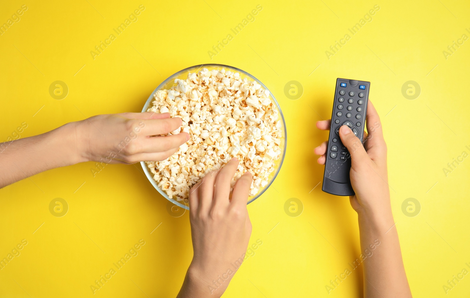 Photo of Women with TV remote eating popcorn on color background, top view. Watching cinema