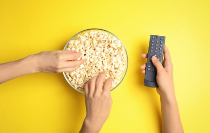 Women with TV remote eating popcorn on color background, top view. Watching cinema