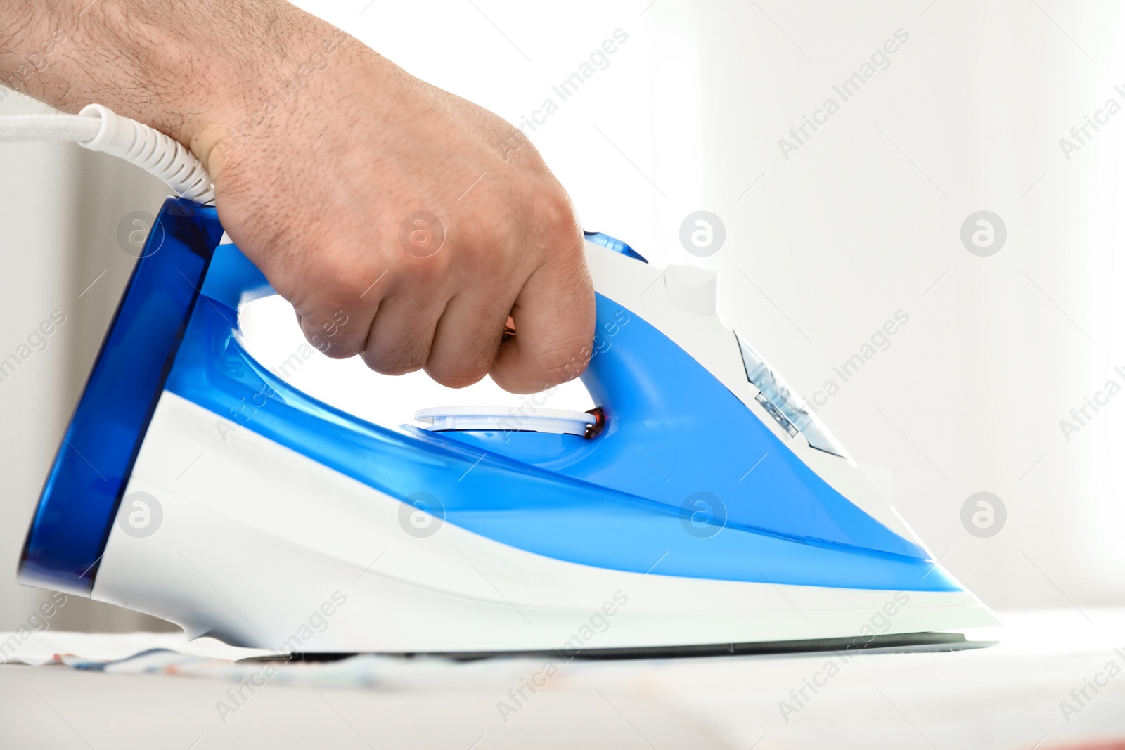 Photo of Man ironing clothes on board indoors. Household chores