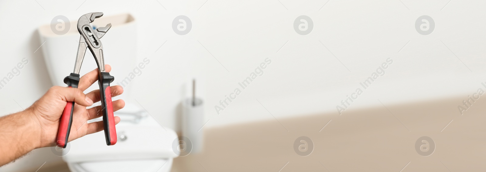 Image of Closeup view of professional plumber holding pliers against toilet bowl in bathroom, space for text. Banner design