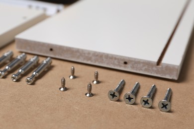 White furniture assembly parts and different metal fasteners on brown background, closeup