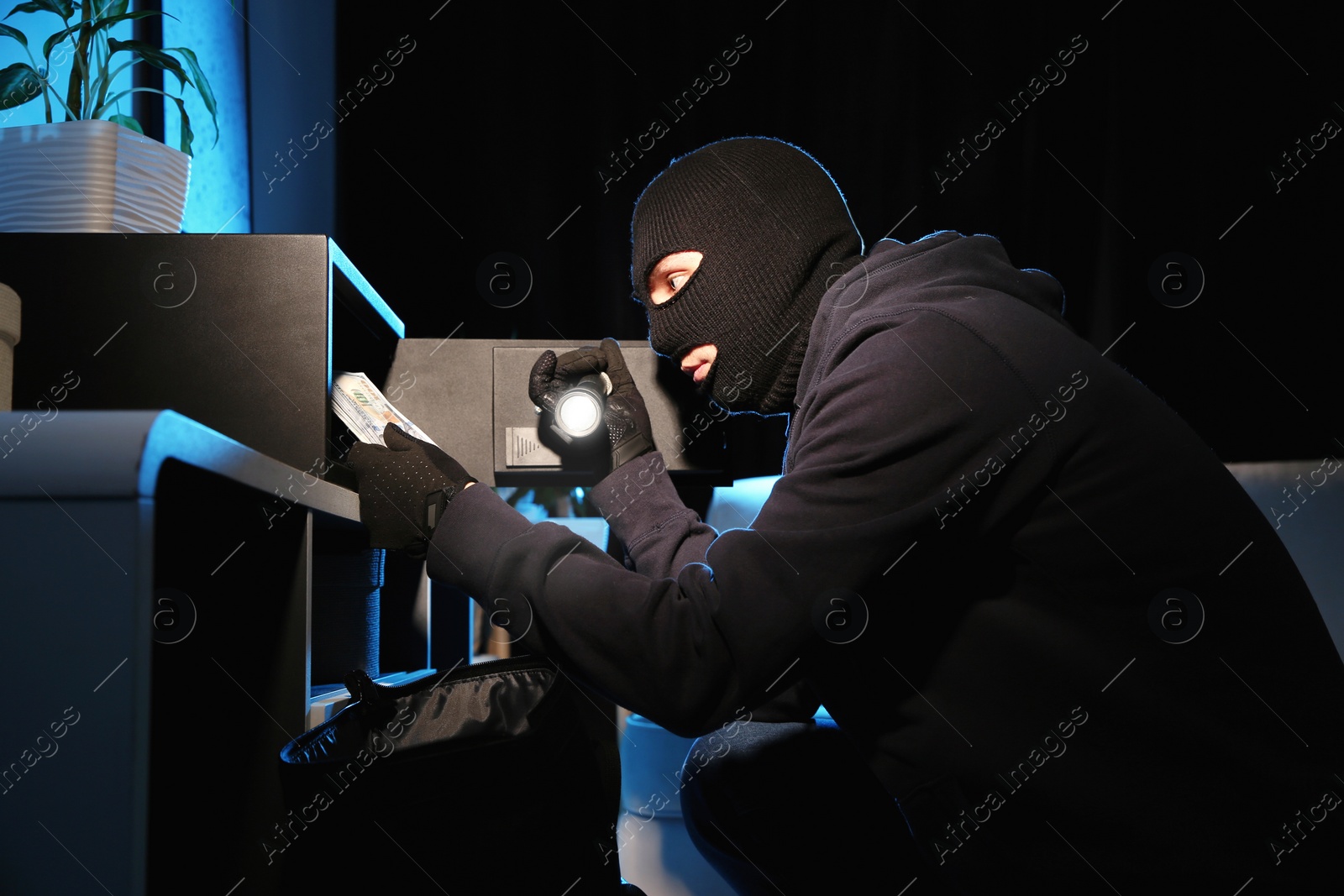 Photo of Thief taking money out of steel safe indoors at night