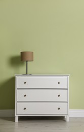 Photo of Modern white chest of drawers with lamp near light green wall indoors