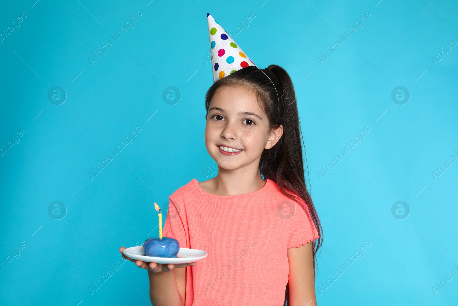 Photo of Happy girl holding birthday sweetness with candle on blue background